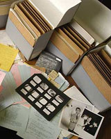 Image of table covered with archival materials: notes, cards, photographs - next to open archive boxes