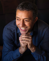 Portrait image of Azouz Begag wearing a dark blue shirt with his arms folded under his chin
