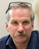 Portrait image of Gregg Mitman wearing a blue shirt (with his glasses on his head)