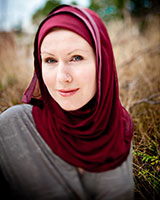 Portrait image of G. Willow Wilson outdoors in a field wearing a grey shirt and a maroon head scarf.