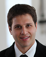 Portrait image of Alexander Angelov wearing a black suit and tie