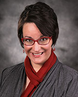 Portrait image of Valerie Barske wearing a grey shirt and red scarf, earrings, and glasses