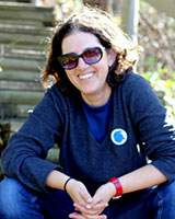 Portrait image of Ayelet Ben-Yishai seated outdoors wearing sunglasses, jeans, and a blue shirt