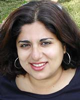 Closely-cropped portrait of Névine El-Nossery outdoors wearing a black shirt and silver hoop earrings