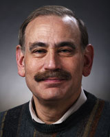 Portrait image of Richard Goodkin with brown hair and mustache wearing a white shirt and dark sweater