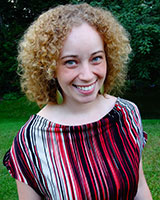 Portrait image of Sarah Groeneveld wearing large green earrings and a red-and-black striped shirt