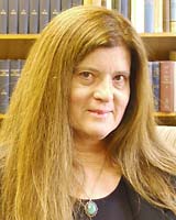 Portrait image of Maria Lepowsky standing in front of book shelves wearing a black shirt and medallion necklace