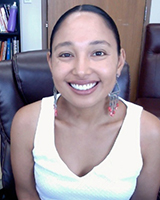 Portrait image of Aida Levy-Hussen wearing a white shirt seated in a black leather chair