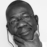 Black and White portrait image of Teju Olaniyan wearing glasses and a light shirt with his hand at his chin.