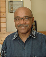Portrait image of Aliko Songolo wearing a blue-grey shirt and glasses
