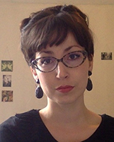Portrait image of Lucy Traverse wearing a black shirt, large black earrings, and tortoise-shell glasses