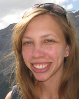 Portrait image of Lisa Woodson outdoors in front of a mountain peak with sunglasses on her head