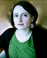 Portrait image of Eliza Zingesser wearing a green shirt, black jacket, and large earrings