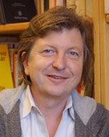 Portrait image of Niklaus Largier in front of bookshelves wearing a grey hooded sweatshirt