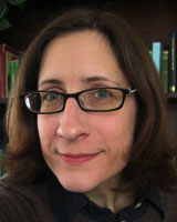 Closely-cropped portrait image of Kristen Ehrhardt wearing a dark shirt and glasses
