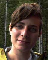 Portrait image of Kristina Kosnick with short hair standing outdoors in a forest wearing a yellow jacket