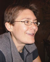 Portrait image of Kate Merz, wearing glasses and a grey shirt around her shoulders, Merz appears to be in the middle of speaking or laughing
