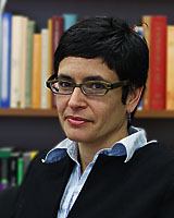 Portrait image of Julia Mickenberg seated in a library wearing a dark jacket, light blue shirt, and glasses