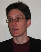 Portrait image of Claire Wendland in front of a white wall wearing a black shirt and glasses
