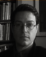Black and White Portrait image of David Williams seated in front of book shelves wearing glasses and a dark shirt