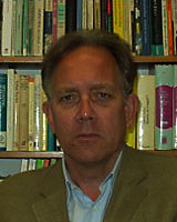 Portrait image of Andre Wink wearing a brown suit jacket and standing in front of book shelves