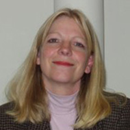 Portrait image of Louise Young in front of a white wall wearing a pink turtle neck and a checkered jacket