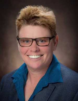 Portrait image of Madelyn Detloff wearing glasses and and blue shirt and grey jacket
