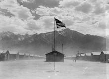 Black and white image of a dust storm at Manzanar War Relocation Authority Center with American Flag at center of image.