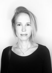 Black and White portrait of Jacquelyn Arcy in front of a white wall.