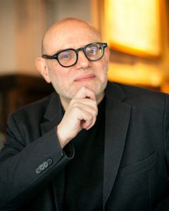 Portrait image of Enzo Traverso with hand on chin wearing a black suit jacket and black shirt.