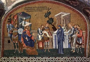 Photograph of a mosaic depicting the "census to collect taxes." Mary and Joseph (shown with halos) appear before a man on a throne, two armed soldiers, and a man writing details on a scroll.