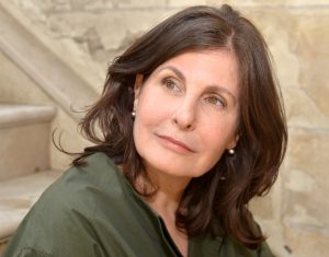 Portrait image of Alice Kaplan seated in front of stone steps wearing a green shirt looking over her right shoulder. She wears her shoulder-length brown hair down