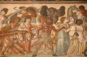 Image of a 3rd-century mosaic depicting a procession of men, women, and animals (including tigers, an elephant, and a giraffe) with a cloven and horned man holding the tigers and a black woman by chains.