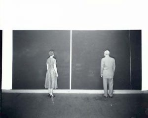 black and white photograph image of a man and woman in 1950s dress standing in front of large single-tone painted canvases with their backs to the photographer