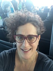 photo portrait or selfie of Rachel Ida Buff wearing dark red glasses and a dark grey/black shirt looking up at the camera