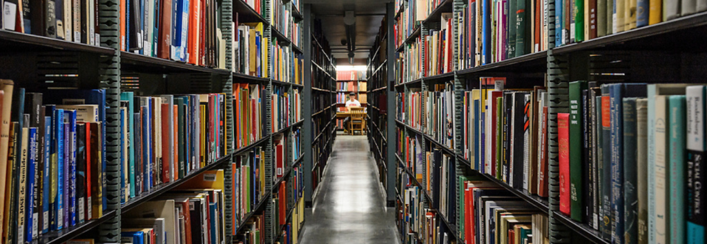 Image of interior of memorial library stacks with dark grey shelves and colorful books stretching into the distance with sharp perspective.