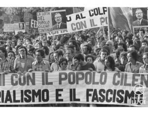 This is a black and white photograph of a group of protestors holding a banner that reads "[With] the Chilean people, [against] imperialism and fascism."