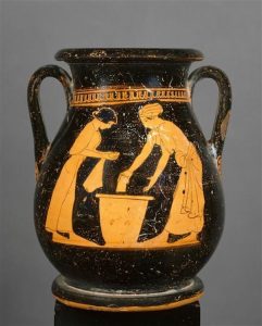 The image features a piece of Greek pottery. It looks like a black vase with two handles near the top. The design on the vase pictures the image of two women leaning over a large vessel. Louvre G547: Red-figure pelike by the Pan painter. 