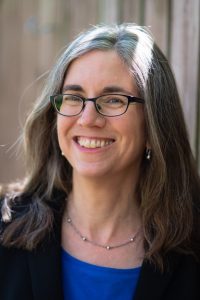 Headshot of Francine Hirsch. She is looking at the camera and smiling. Francine is wearing black glasses, a silver necklace, and matching earrings. Her hair is loose and falls slightly past her shoulders. She is wearing a blue shirt under a black blazer.