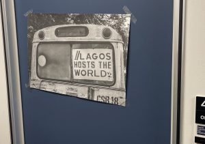 Image of a black and white poster taped to a blue wall. The photo depicts an older bus with a poster in the window that reads "Lagos hots the world"