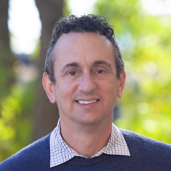 Image of Robert in front of greenery. He has short hair and is wearing a blue sweater with a collared shirt underneath.