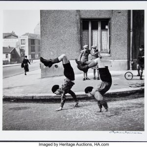 Black and white image of two boys wearing matching outfits and walking on their hands.