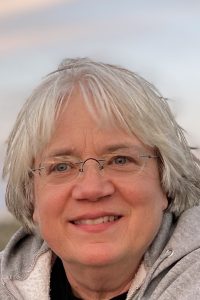 1.This is a head shot of a smiling woman with grey hair and wire rim glasses. 