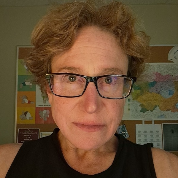 This is a headshot of a woman with short light-brown hair and glasses, wearing a black sleeveless shirt.