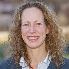 Image of woman with fair skin and curly light brown hair wearing a collared shirt under a blue sweater.