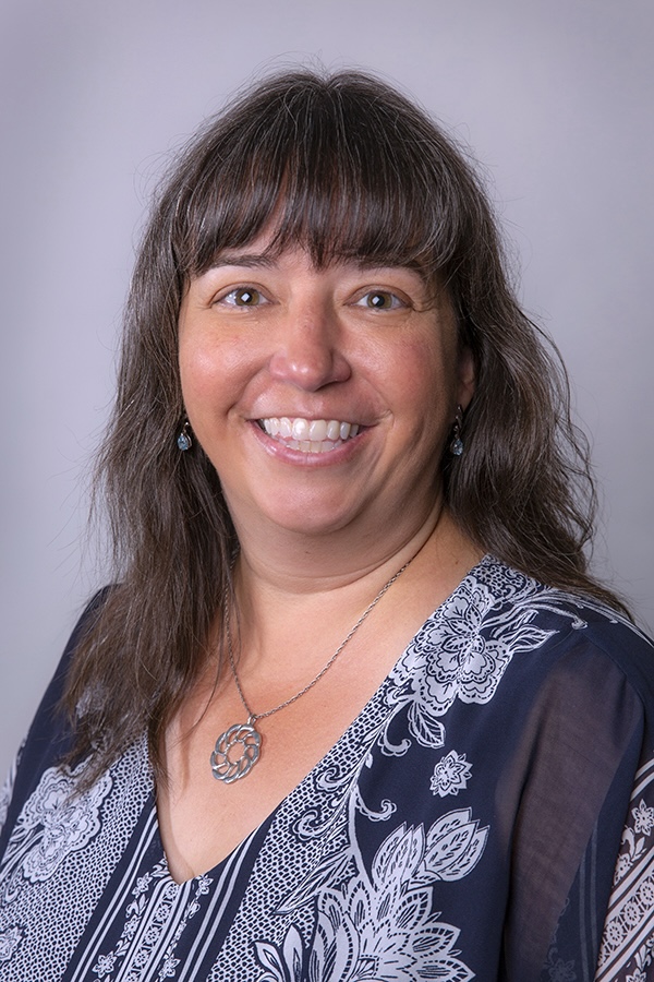 This is a headshot of a smiling woman with shoulder-length brown hair.