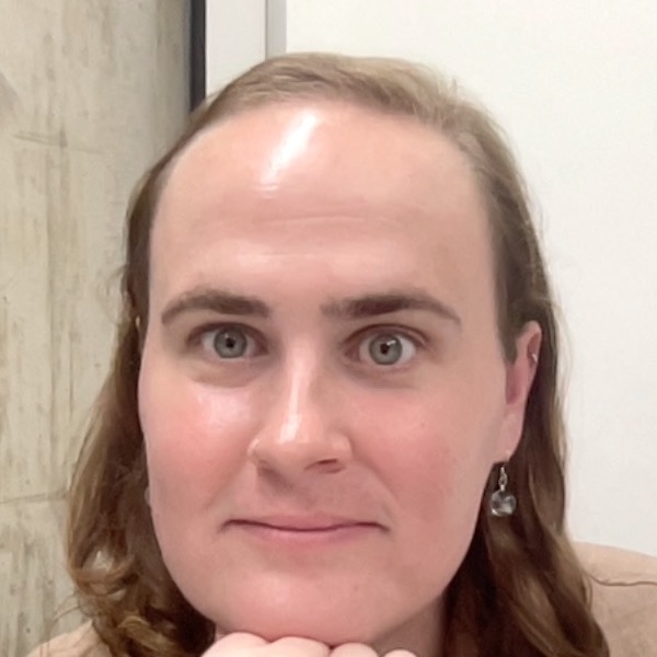 This is a headshot of a person in an office. They have short brown hair and are wearing dangly earrings.