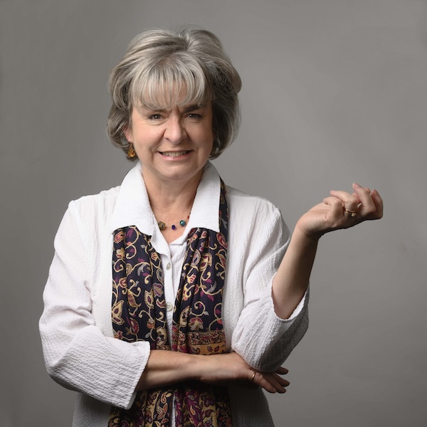 This is a headshot of a woman with short brown hair in a white shirt standing in front of a brown background.