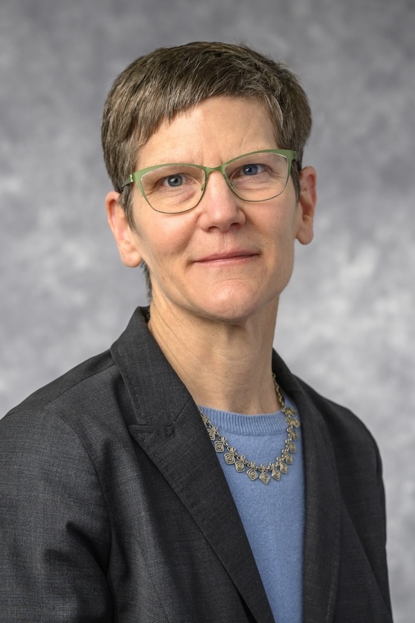 This is a color headshot of a woman with short brown hair with a studio-grey background.