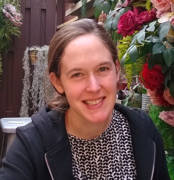 Or, if my preferred photo can be used instead, This is a picture of a woman with brown hair sitting outside in front of greenery and flowers.
